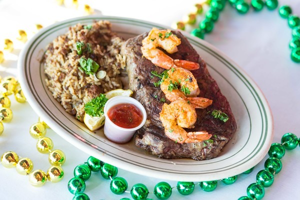 Grilled steak topped with seasoned shrimp, dirty rice, and dipping sauce